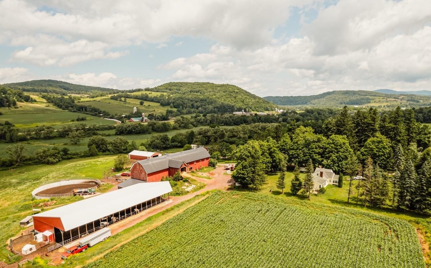 Ashridge farm acreage — aerial view of red barns and white farmhouse among fields and forest, South Kortright, New York