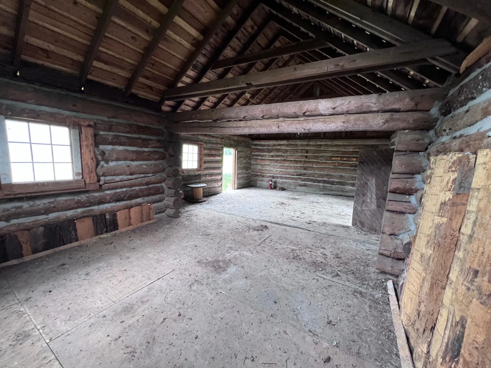 Wider interior of the boathouse showing multi-pane windows, exposed log walls and open roof trusses.
