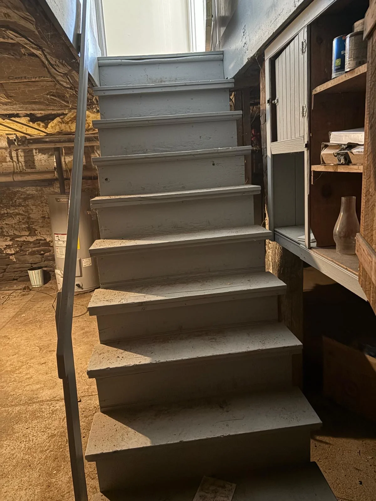Painted wooden stair down into the farmhouse cellars — stone walls and a built-in cupboard at the landing.