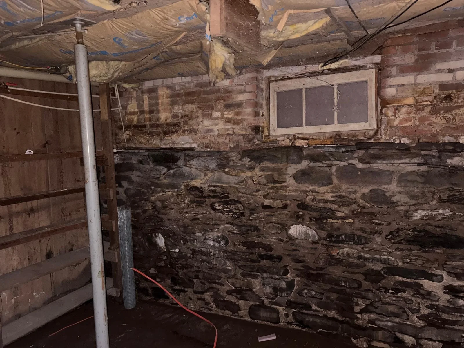 Cellar wall of rough stone below original brick, with a small below-grade window.