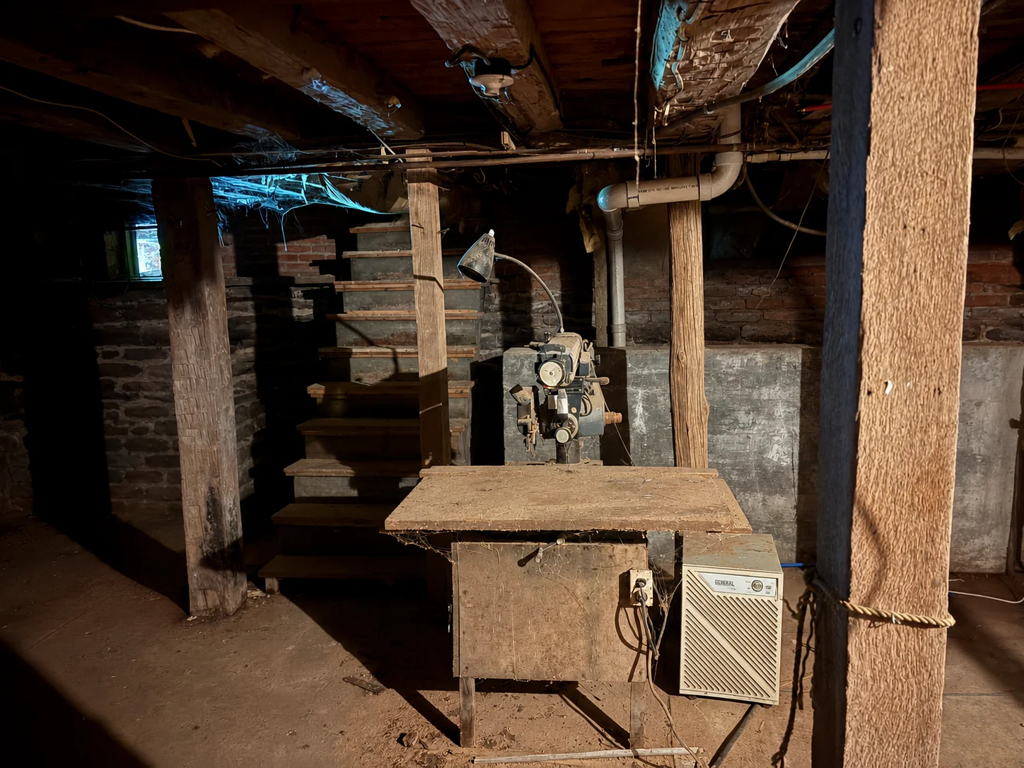 The cellar workshop — old saw bench, timber posts, and the stone stair beyond (digitally cleared reference).
