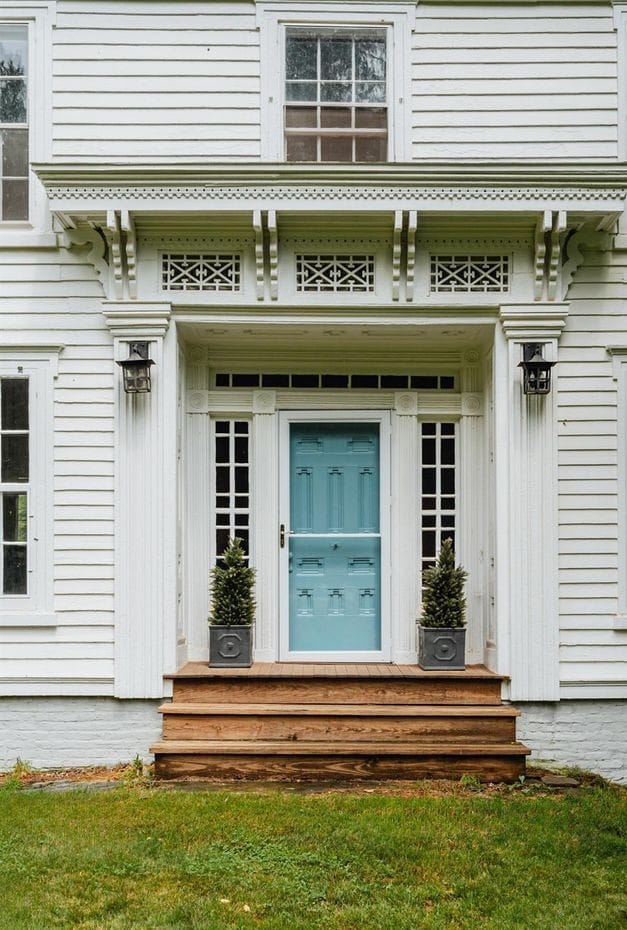 Greek Revival farmhouse front entry — blue paneled door, sidelights, transom, and ornate brackets, South Kortright, New York