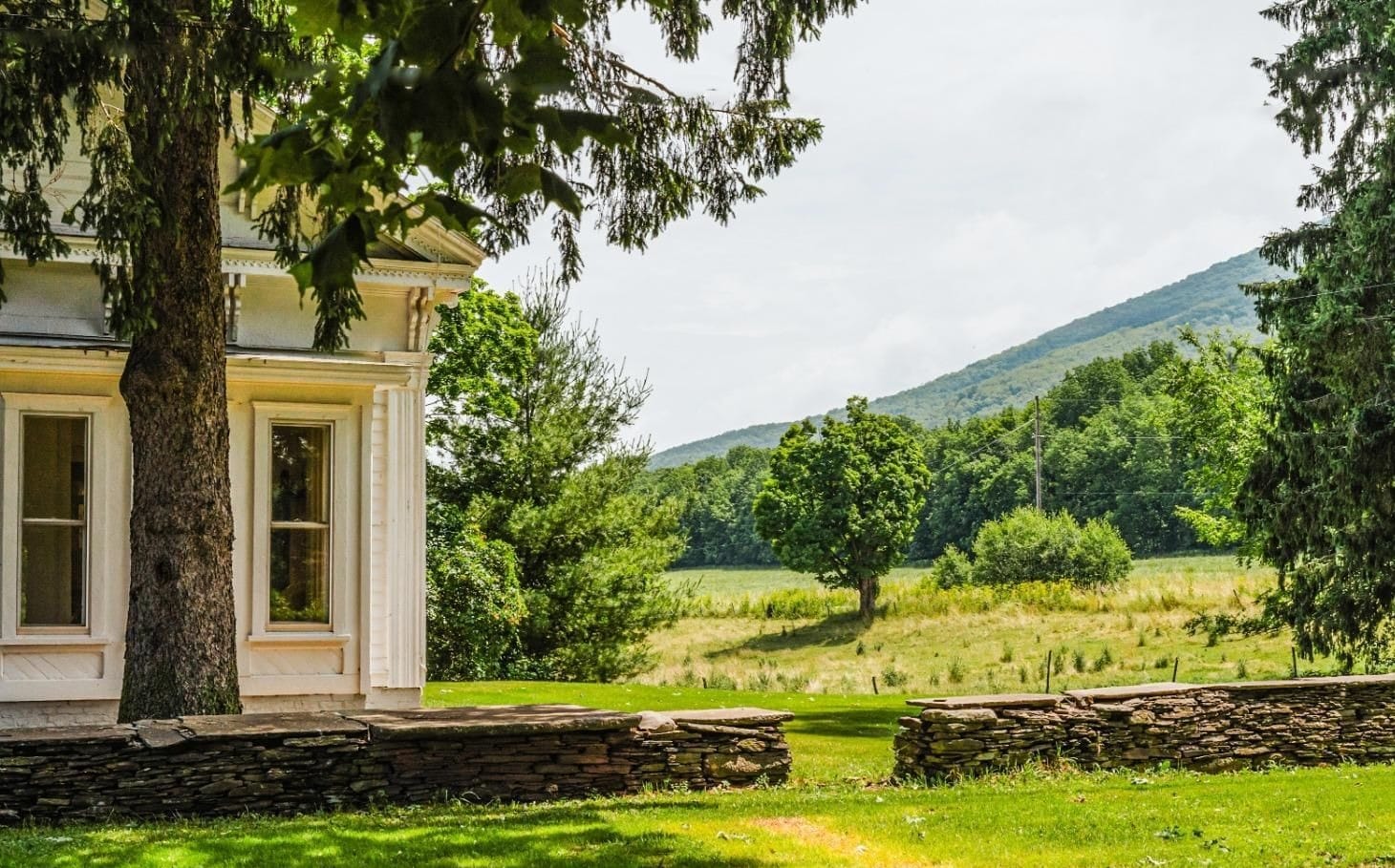 Greek Revival farmhouse with dry-stack stone wall and mountain backdrop, South Kortright, New York