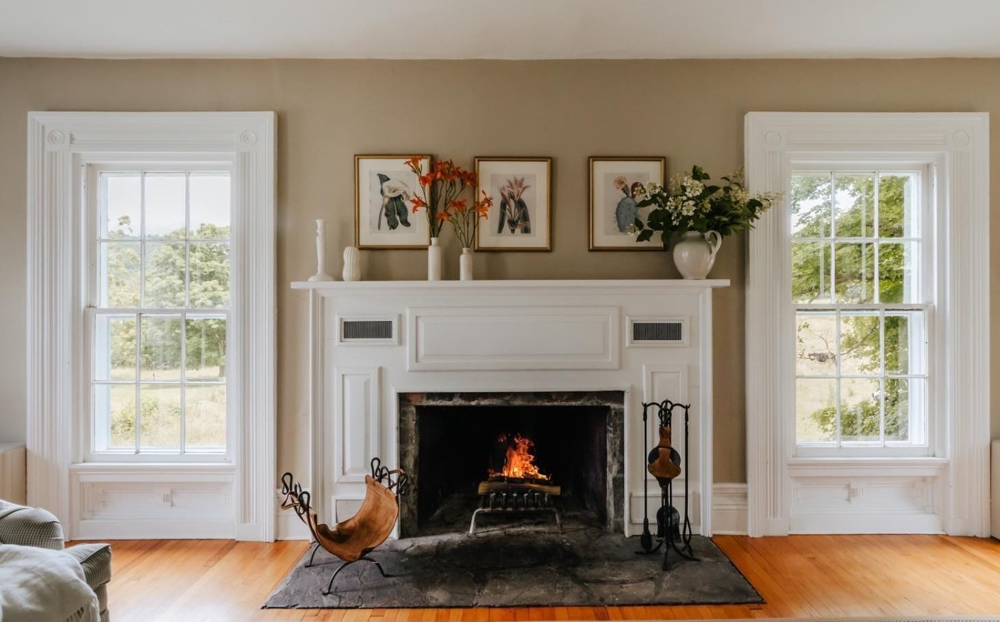 Farmhouse living room at Ashridge Estate — lit stone fireplace, hardwood floors, and botanical prints, South Kortright, New York