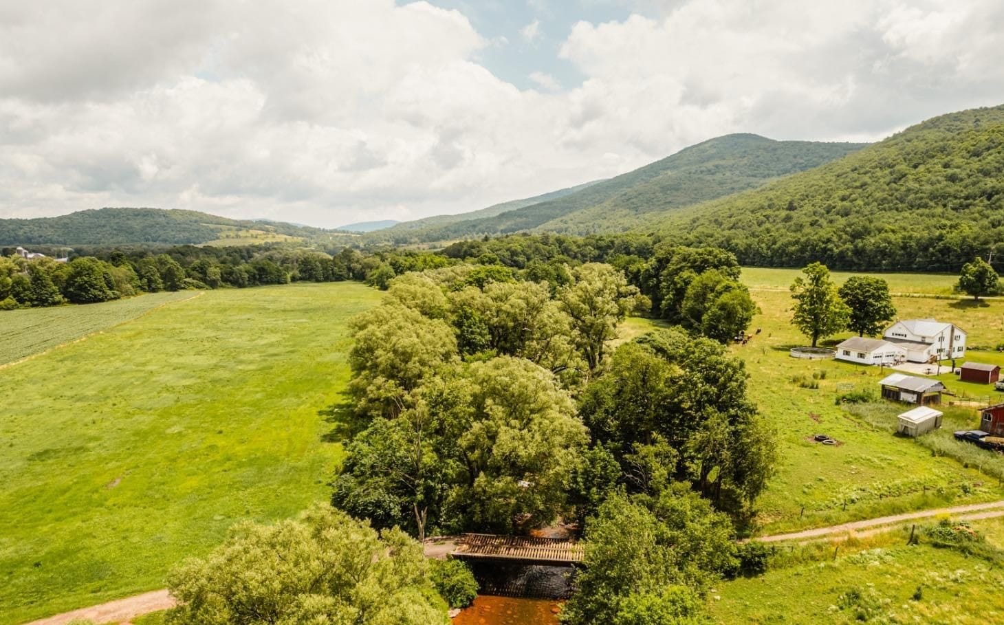 Ashridge farm acreage — aerial view of the Greek Revival farmhouse, red barns, stream, and Catskill valley, South Kortright, New York