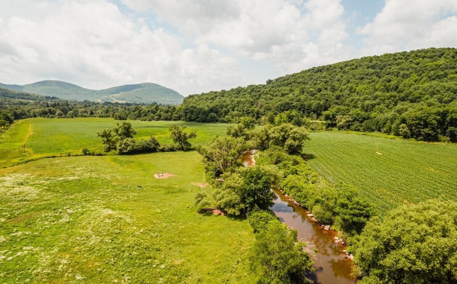 Ashridge estate — aerial view of river valley, meadow, crop rows, and forested Catskill mountains, South Kortright, New York