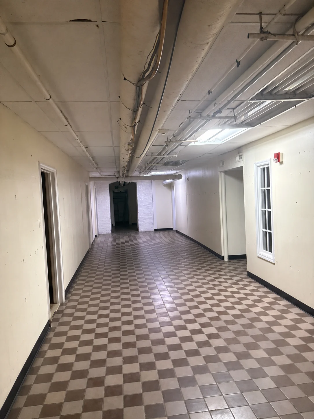 Long lower-level corridor — checkerboard tile floor and doorways receding toward an arched opening.