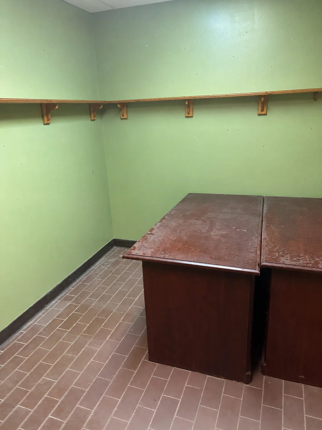 Green room with wooden desks and a shelf rail — reads as a classroom or period office.