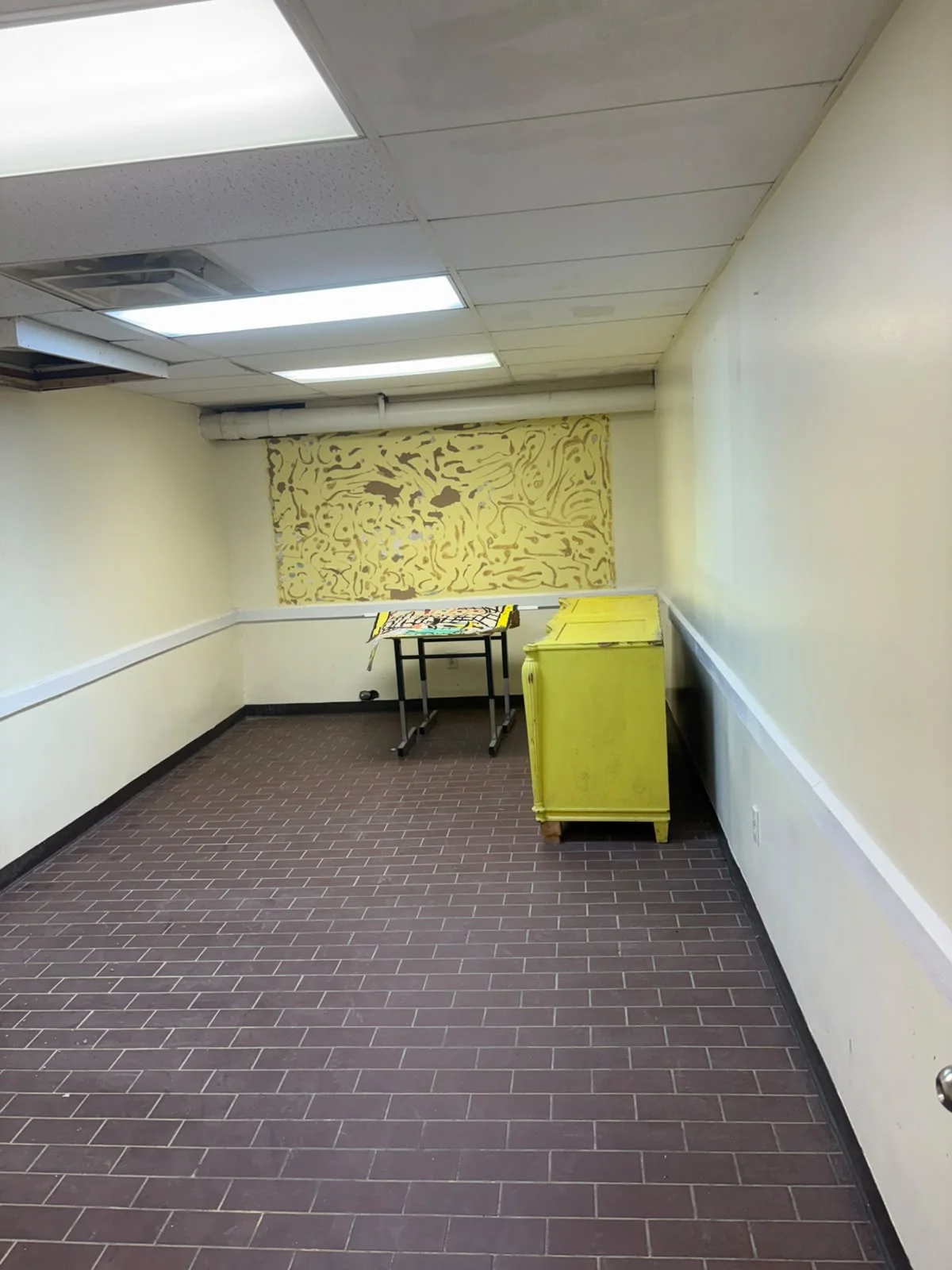 Tiled room with fluorescent panels, chair rail, a school desk, and a painted dresser.