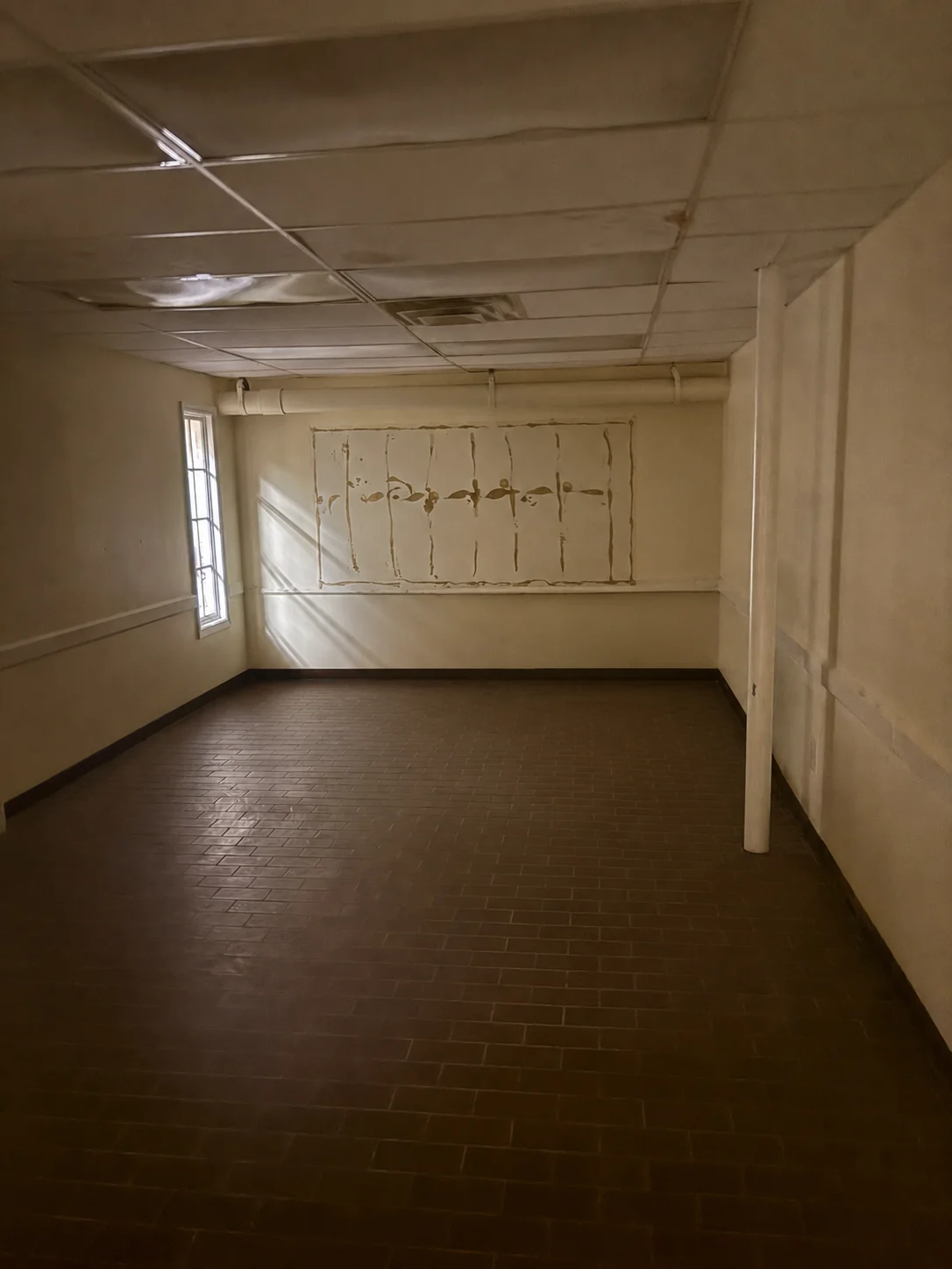 Room with a divided-lite window and a wallpaper-remnant panel — natural light below grade (digitally cleared reference).