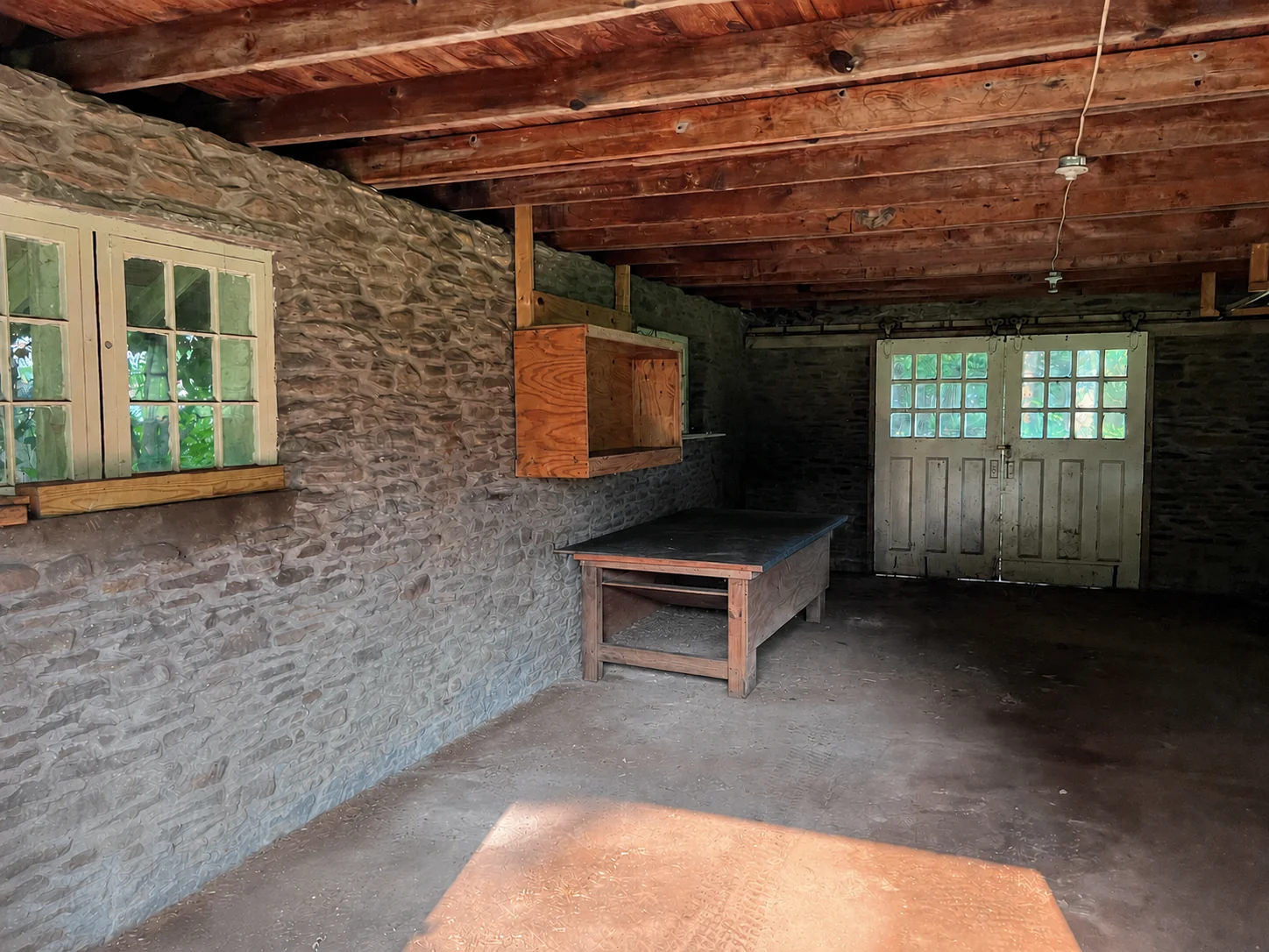 Inside the stone house — a single open room with stone walls, exposed timber joists, multi-pane windows, and carriage doors (digitally cleared reference).