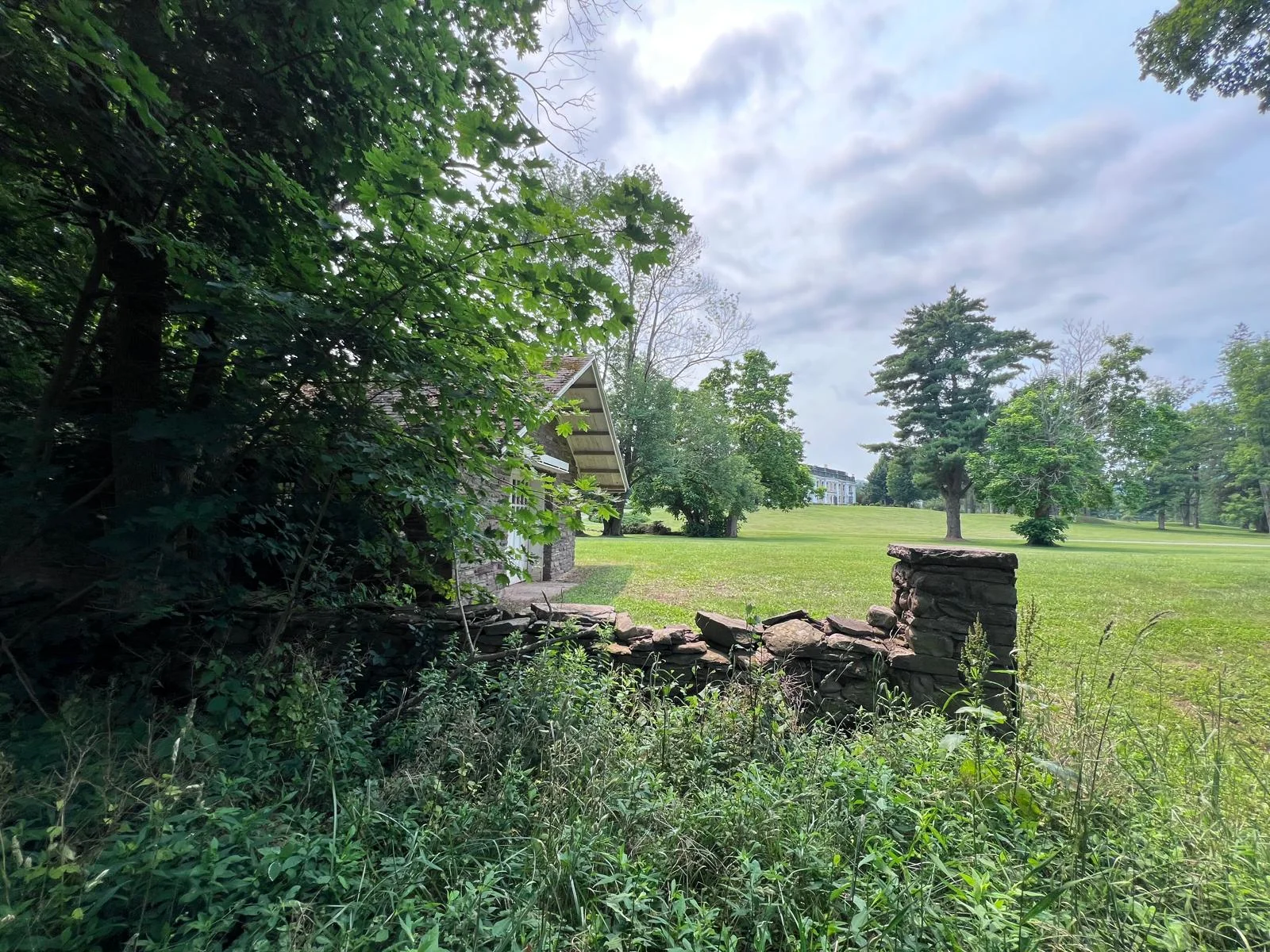 The stone house behind its old stone wall, with open lawn and the mansion visible in the distance.